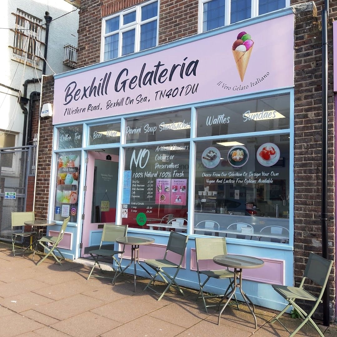 The Bexhill Gelateria shopfront on Western Road: a lilac sign with an ice-cream cone, pale blue window frames lettered with coffee, tea, beer, wine, panini, soup, sandwiches, waffles and sundaes, and café tables on the pavement